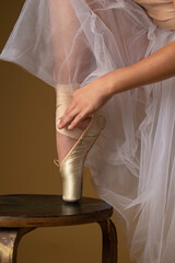 Ballerina straightens her pointe shoes on a beige background in a chopin skirt, ballet tutu on a wooden chair