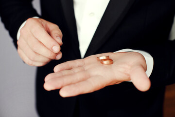 Obraz premium Preparing for wedding. Groom buttoning cufflinks on white shirt before wedding. Groom's clothes. Close up.