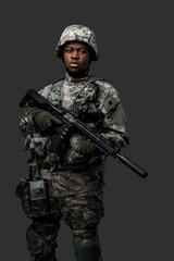 Photo of handsome military man of african ethnic armed with rifle isolated on gray.