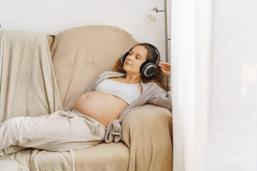  Happy young pregnant woman listening to music in headphones