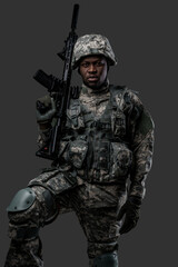 Combative african soldier with serious face holding rifle looking at camera against dark background.