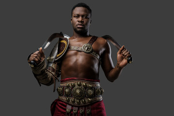 Shot of antique gladiator of african descent holding dual swords isolated on gray background.