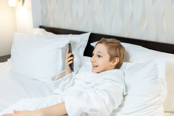 Obraz na płótnie Canvas a boy in a hotel room lies on the bed holding a phone in front of him and talking on the speakerphone on the phone