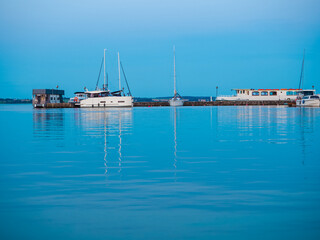 waterfront view on jetty with moored sailing yacht and motorboat, calm blue dusk waterscape
