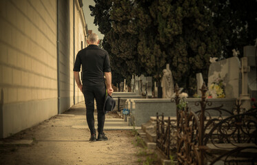 Adult man in black holding hat mourning in cemetery