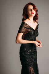 Fototapeta premium Ginger woman in maxi black gown. Candid portrait. Transparent slim shiny dress with v neckline. Stunning look for an event, female fashion. Sexy outfit. Dramatic studio portrait.