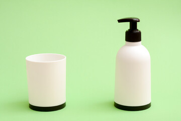 White liquid soap bottle and a cup on green background.