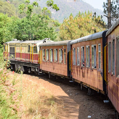 Obraz premium Toy Train moving on mountain slopes, beautiful view, one side mountain, one side valley moving on railway to the hill, among green natural forest. Toy train from Kalka to Shimla in India