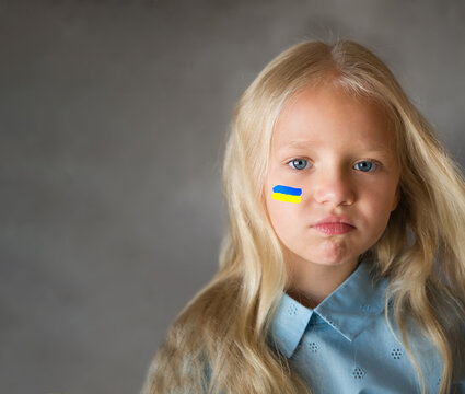 
Portrait of a Ukrainian girl with a painted flag on her cheek in yellow and blue tones of the Ukrainian flag. Peace and child protection concept