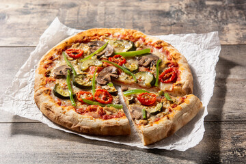 Vegetarian pizza with zucchini, tomato, peppers and mushrooms on wooden table