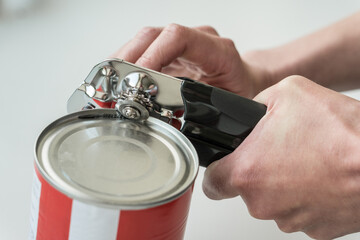 Hands opening a can in a kitchen with a tin opener.