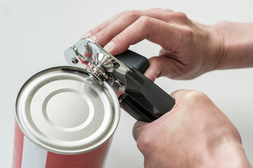 Hands opening a can in a kitchen with a tin opener. - 508414093