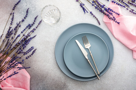 Table setting, empty plate with napkin and cutlery on a gray-pink concrete background, top view of the served table decorated with dry lavender flowers