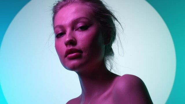 Close-up with a slow-motion approach to the face of a pretty, stylish girl with makeup. The young woman is illuminated by a multicolor RGB light.