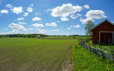 Rural landscape on a beautiful spring day in Rusko, Finland. A traditional Finnish roundpole fence runs around the old barn.