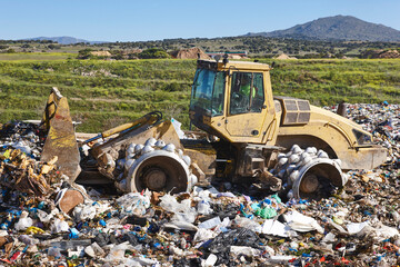 Fototapeta na wymiar Heavy machinery shredding garbage in an open air landfill. Pollution