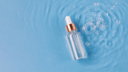 Glass bottle of anti aging serum and falling water drops on blue background