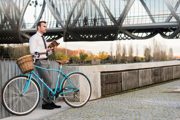 Business man with vintage bicycle by the river reading a book