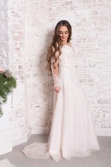 The bride in full growth, against the backdrop of a white brick wall.