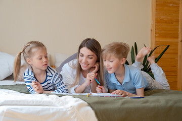 Mother and her two children drawing together at home laying on bed sofa. Son and daughter spend time with their mom. Cute happy family leisure. Boy and girl with parent together