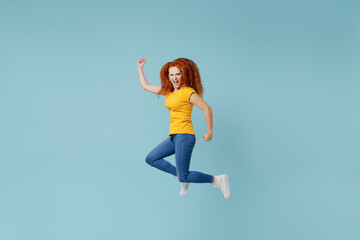 Fototapeta na wymiar Side view full body young smiling happy redhead woman 20s wearing yellow t-shirt jump high do winner gesture isolated on plain light pastel blue background studio portrait. People lifestyle concept.