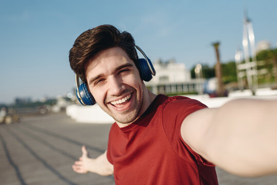 Close up young strong sporty fit sportsman man in t-shirt headphones do selfie shot mobile cell phone show place warm up train at sunrise sun dawn over sea beach outdoor on pier seaside in morning.