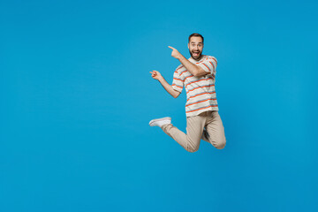 Full body young smiling fun man 20s in orange striped t-shirt jump high point index finger aside on workspace area mock up isolated on plain blue background studio portrait. People lifestyle concept.