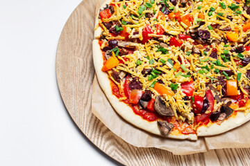Close-up top view of homemade vegan pizza on wooden plate on white background.