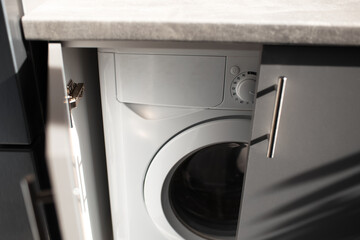 Close-up of washing machine inside kitchen cabinet with opened doors. Top view.