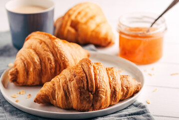 Plate with fresh croissants, jam and coffee on white wooden table. Close up.