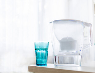 Water filter jug and blue glass with water on light blurred background. Healthy lifestyle. Ecology.