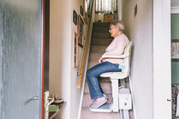 Senior woman using automatic stair lift on a staircase at her home. Medical Stairlift for disabled...