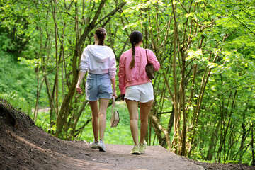 Obraz premium Two girls in denim shorts walking in a summer park, rear view. Concept of female friendship, hot weather