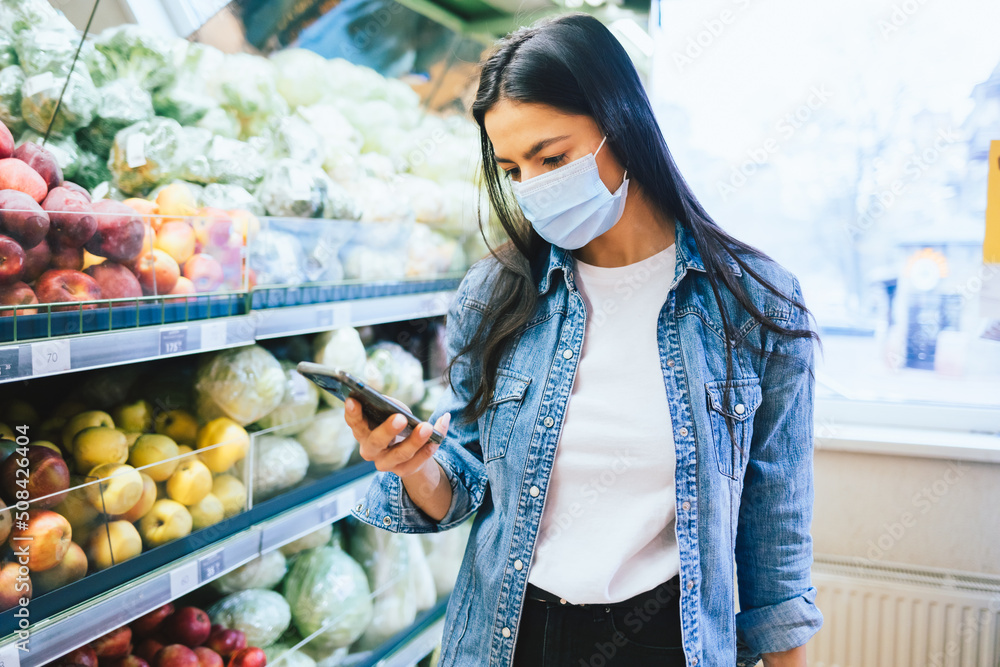 Wall mural Brunette girl wearing protective mask uses smartphone