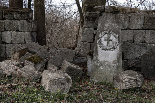 A demolished stone wall with a damaged tombstone in a cemetery