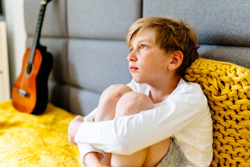 Lonely sad preteen boy sitting on couch at home. Autism concept. Offended boy sitting on sofa at...