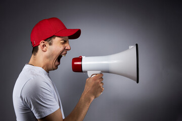 Fototapeta premium A teenager in an orange construction helmet with a loudspeaker in his hand on a dark background shouts into a megaphone