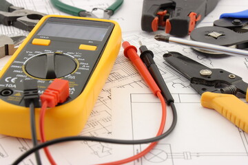 Multimeter and tools for installing an electrical control panel in close-up on an electrical diagram.