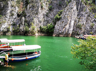 Fototapeta na wymiar Journey to the Matka canyon in Macedonia. Emerald water in the lake, many tourist boats against the backdrop of high rocks and mountains. A man enters the water on the steps 