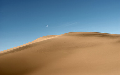 Desert landscape. Moon against blue sky over sand dunes