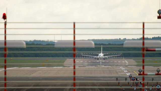 Long shot view over the airport fence, a passenger jet with an unrecognizable livery taxis onto the runway strat before takeoff. Tourism and travel concept
