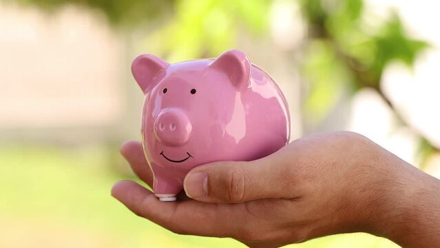 Dinheiro, Real Brasileiro. Um homem jovem segurando um cofrinho e colocando moedas do Real Brasileiro - BRL. Conceitos de guardar dinheiro e investimentos.