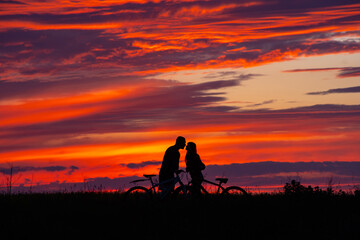 Fototapeta na wymiar Side view of couple riding on bicycles. sunset sky on background. couple in love. silhouette of man and woman. Romance concept