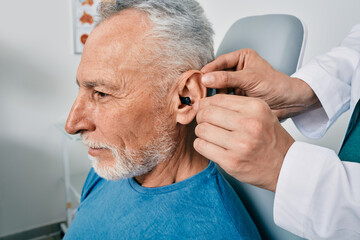 Grey-haired elderly man during installation intra-ear hearing aid into his ear by his doctor...