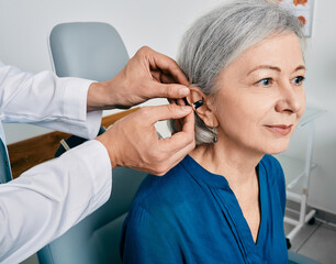 Senior woman during installation hearing aid into her ear by her audiologist, close-up. Hearing...