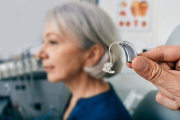 Close-up of hearing aid near senior patient's ear at audiology clinic. Hearing solutions, hearing...