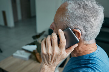 Elderly man with hearing aid has a full life and can hear interlocutor on phone. Hearing solution and innovation technology