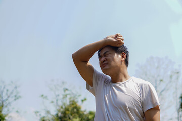 Asian middle-aged man feels hot, stands outdoor in sunny day. Concept : hot weather in summer, high...