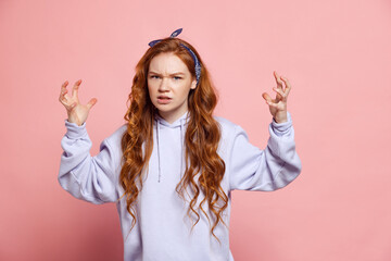 Angry young redhead girl, student looking at camera isolated on pink studio background. Human emotions, facial expression concept. Trendy colors