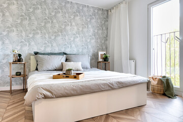 Modern interior of bedroom with window, wooden floor and comfortable double bed with pillows sheets and blanket. Cozy interior for rest and trendy design. - obrazy, fototapety, plakaty